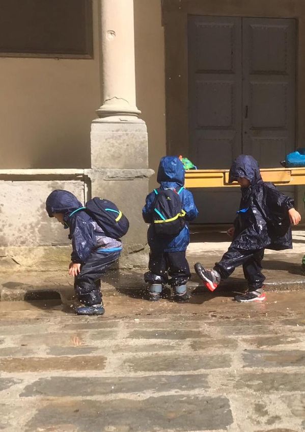Bambini con le tute antipioggia che giocano tra le pozzanghere in città.